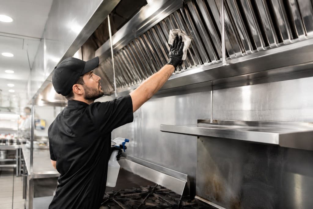 Technician cleaning commercial kitchen vent hood baffle filters in a restaurant kitchen