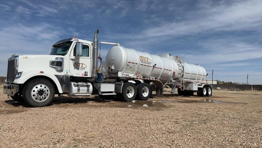 White semi truck with silver tanker trailer ready for heavy equipment cleaning