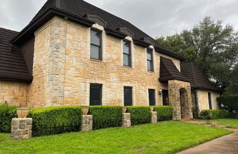 Large stone home with clean exterior siding and dark roof after soft washing